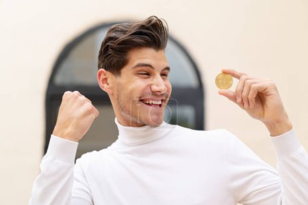 Photo for Young caucasian man holding a Bitcoin at outdoors celebrating a victory - Royalty Free Image