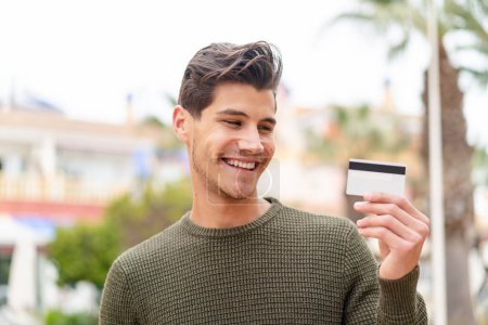 Photo for Young caucasian man holding a credit card at outdoors with happy expression - Royalty Free Image