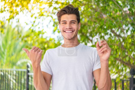 Photo for Young caucasian man holding invisible braces at outdoors pointing to the side to present a product - Royalty Free Image