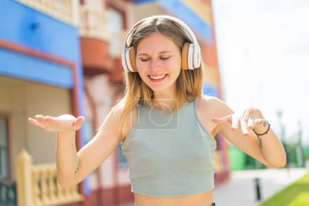 Téléchargez les photos : Jeune femme blonde à l'extérieur écouter de la musique et danser - en image libre de droit