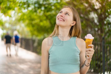 Foto de Joven rubia bonita mujer con un helado de corneta al aire libre mirando hacia arriba mientras sonríe - Imagen libre de derechos