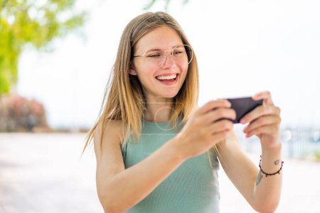 Téléchargez les photos : Jeune femme blonde en plein air jouant avec le téléphone mobile - en image libre de droit