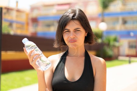Téléchargez les photos : Jeune jolie femme bulgare avec une bouteille d'eau à l'extérieur avec une expression triste - en image libre de droit