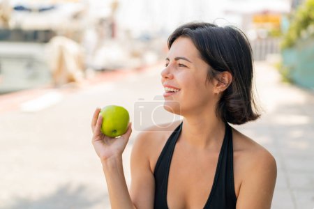 Photo for Young pretty Bulgarian woman at outdoors with an apple and happy - Royalty Free Image