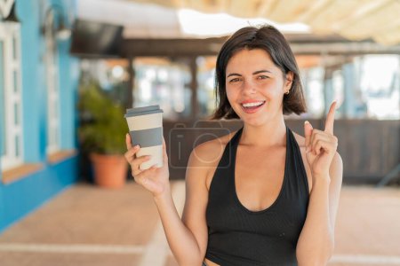 Foto de Joven bonita mujer búlgara sosteniendo un café para llevar al aire libre señalando una gran idea - Imagen libre de derechos
