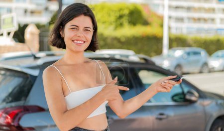 Téléchargez les photos : Jeune jolie femme bulgare à l'extérieur tenant des clés de voiture avec une expression heureuse - en image libre de droit