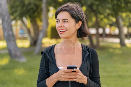 Foto de Joven bonita mujer búlgara al aire libre utilizando el teléfono móvil y mirando hacia arriba - Imagen libre de derechos