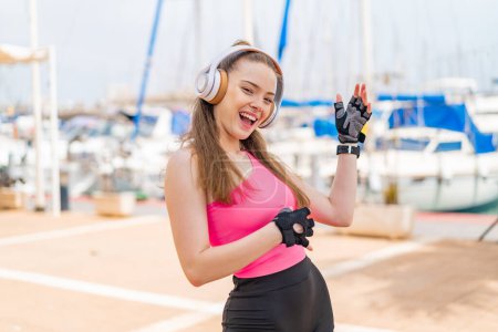Téléchargez les photos : Jeune jolie fille sportive à l'extérieur écouter de la musique et faire un geste de guitare - en image libre de droit