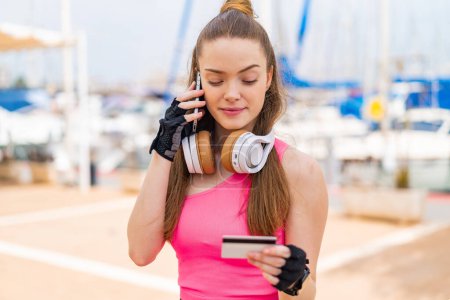 Photo for Young pretty sport girl at outdoors buying with the mobile with a credit card - Royalty Free Image