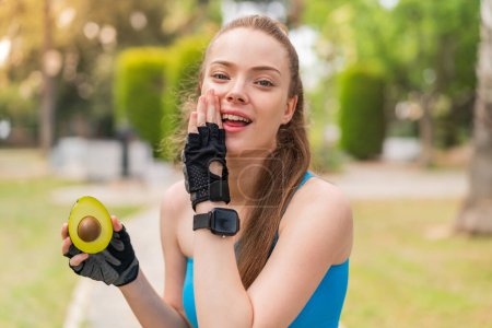 Photo for Young pretty sport girl holding an avocado at outdoors whispering something - Royalty Free Image