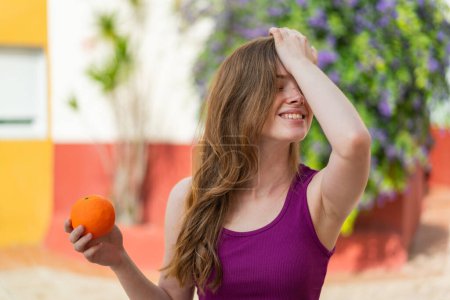 Téléchargez les photos : Jeune rousse femme tenant une orange à l'extérieur a réalisé quelque chose et l'intention de la solution - en image libre de droit