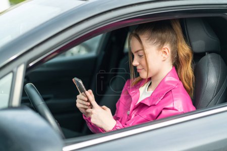 Téléchargez les photos : Jeune jolie fille à l'intérieur d'une voiture en utilisant un téléphone mobile - en image libre de droit