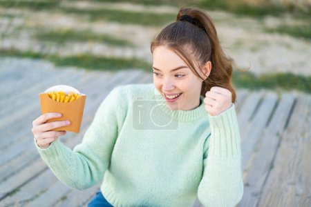 Téléchargez les photos : Jeune jolie fille tenant des chips frites à l'extérieur célébrant une victoire - en image libre de droit