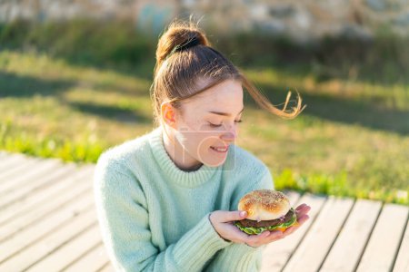 Téléchargez les photos : Jeune jolie fille tenant un hamburger à l'extérieur - en image libre de droit