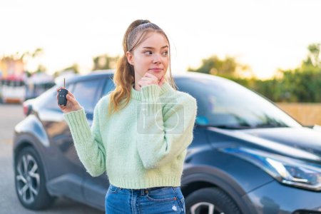 Téléchargez les photos : Jeune jolie fille tenant des clés de voiture à l'extérieur pensant une idée et regardant côté - en image libre de droit