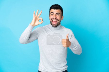 Photo for Caucasian man over isolated blue background showing ok sign and thumb up gesture - Royalty Free Image
