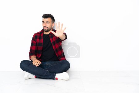Foto de Joven hombre guapo sentado en el suelo contando cinco con los dedos - Imagen libre de derechos