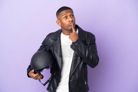 Photo for Latin man with a motorcycle helmet isolated on purple background having doubts while looking up - Royalty Free Image