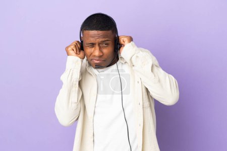Foto de Hombre latino telemarketer trabajando con un auricular aislado sobre fondo morado frustrado y cubriendo orejas - Imagen libre de derechos