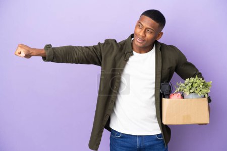 Foto de Hombre latino haciendo un movimiento mientras recoge una caja llena de cosas dando un gesto de pulgar hacia arriba - Imagen libre de derechos