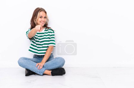 Photo for Young Russian girl sitting on the floor isolated on white background points finger at you with a confident expression - Royalty Free Image