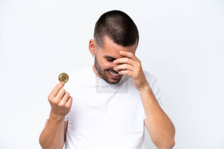 Foto de Joven hombre caucásico sosteniendo un bitcoin aislado sobre fondo blanco riendo - Imagen libre de derechos