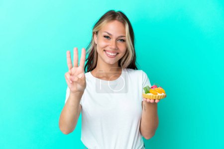 Photo for Young Russian woman holding a fruit sweet isolated on blue background happy and counting three with fingers - Royalty Free Image