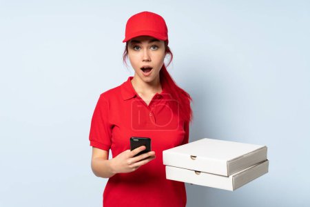 Téléchargez les photos : Pizza livraison fille tenant une pizza sur fond isolé surpris et l'envoi d'un message - en image libre de droit
