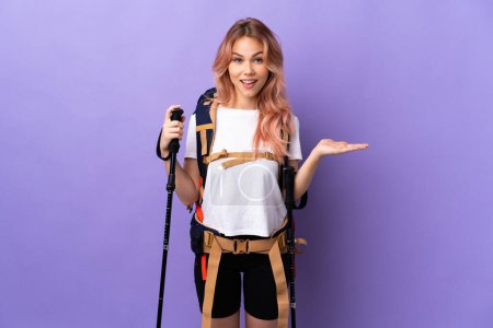 Foto de Chica adolescente con mochila y bastones de trekking sobre fondo púrpura aislado con expresión facial impactada - Imagen libre de derechos