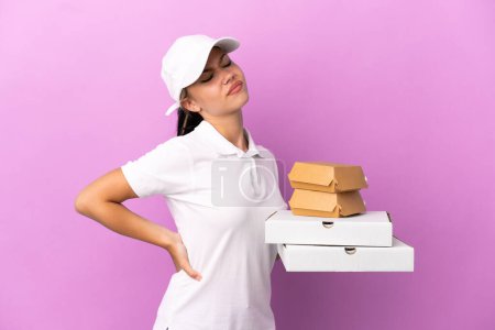 Photo for Pizza delivery Russian girl with work uniform picking up pizza boxes and burgers isolated on purple background suffering from backache for having made an effort - Royalty Free Image