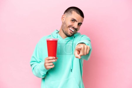 Téléchargez les photos : Jeune homme caucasien tenant soda isolé sur fond rose pointant devant avec expression heureuse - en image libre de droit