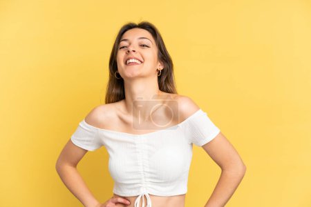 Photo for Young caucasian woman isolated on yellow background posing with arms at hip and smiling - Royalty Free Image