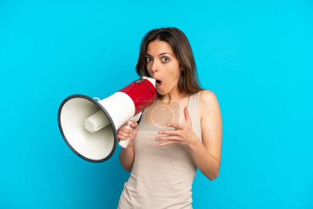 Téléchargez les photos : Young caucasian woman isolated on blue background shouting through a megaphone with surprised expression - en image libre de droit