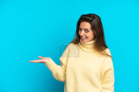 Téléchargez les photos : Jeune femme caucasienne isolée sur fond bleu présentant une idée tout en regardant souriant vers - en image libre de droit