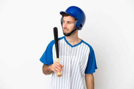 Téléchargez les photos : Jeune homme caucasien jouant au baseball isolé sur fond blanc regardant vers le côté et souriant - en image libre de droit