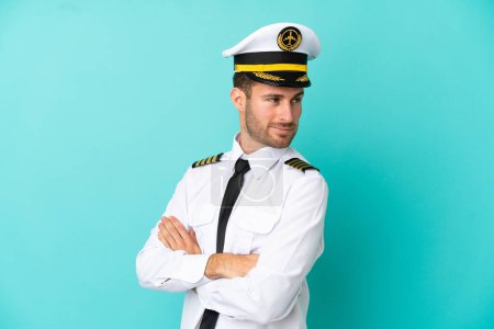Photo for Airplane caucasian pilot isolated on blue background with arms crossed and happy - Royalty Free Image