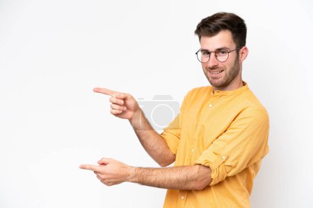 Foto de Joven hombre caucásico aislado sobre fondo blanco apuntando con el dedo hacia un lado y presentando un producto - Imagen libre de derechos