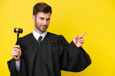 Téléchargez les photos : Juge caucasien homme isolé sur fond jaune pointant doigt sur le côté - en image libre de droit