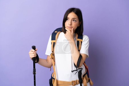 Photo for Young caucasian woman with backpack and trekking poles isolated on blue background having doubts - Royalty Free Image