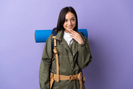 Téléchargez les photos : Jeune alpiniste femme avec un grand sac à dos sur fond isolé levant les yeux tout en souriant - en image libre de droit
