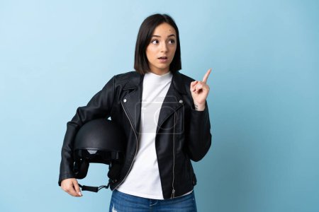Foto de Mujer sosteniendo un casco de moto aislado sobre fondo azul pensando en una idea apuntando con el dedo hacia arriba - Imagen libre de derechos