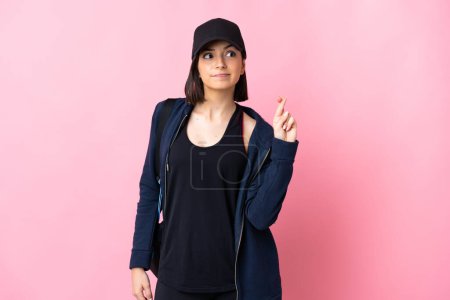 Téléchargez les photos : Jeune femme sportive avec sac de sport isolé sur fond rose avec les doigts croisés et souhaitant le meilleur - en image libre de droit