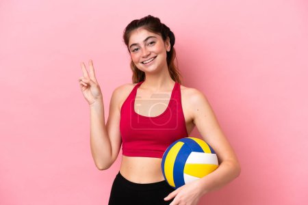 Téléchargez les photos : Jeune femme caucasienne jouant au volley isolé sur fond rose souriant et montrant signe de victoire - en image libre de droit
