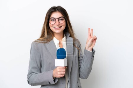 Téléchargez les photos : Jeune présentateur de télévision caucasienne femme isolée sur fond blanc souriant et montrant signe de victoire - en image libre de droit