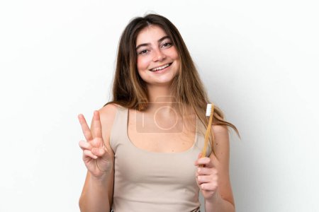 Foto de Mujer joven caucásica cepillándose los dientes aislados sobre fondo blanco sonriendo y mostrando signo de victoria - Imagen libre de derechos