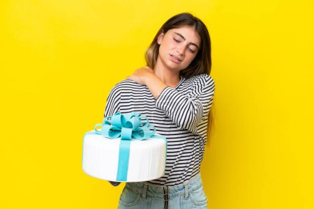 Young caucasian woman holding birthday cake isolated on yellow background suffering from pain in shoulder for having made an effort