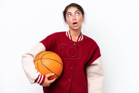 Foto de Joven jugador de baloncesto mujer aislada sobre fondo blanco mirando hacia arriba y con expresión sorprendida - Imagen libre de derechos