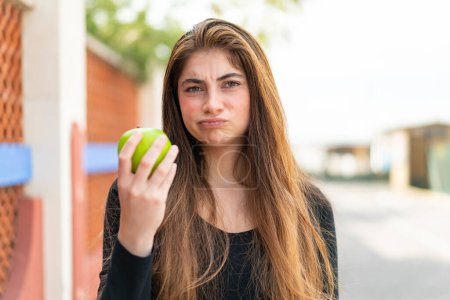 Photo for Young pretty caucasian woman with an apple at outdoors with sad expression - Royalty Free Image