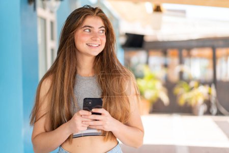 Téléchargez les photos : Jeune jolie femme caucasienne utilisant le téléphone mobile et levant les yeux - en image libre de droit