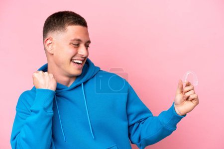 Photo for Young Brazilian man holding invisible braces isolated on pink background celebrating a victory - Royalty Free Image